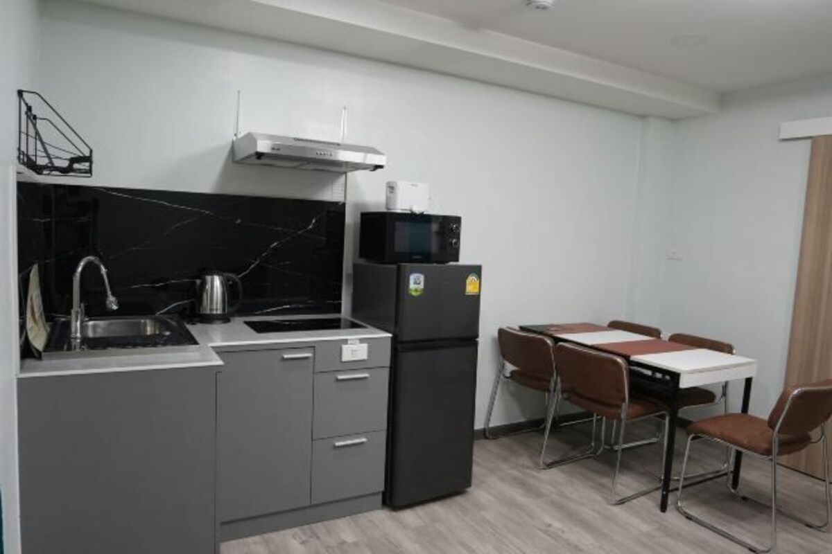 A compact kitchen with a sink, stove, and microwave. There is a dining area with a table and chairs.