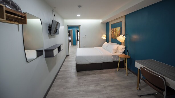 Une chambre d’hôtel moderne équipée d’un lit, d’une table de chevet, d’une lampe et d’un téléviseur fixé au mur.