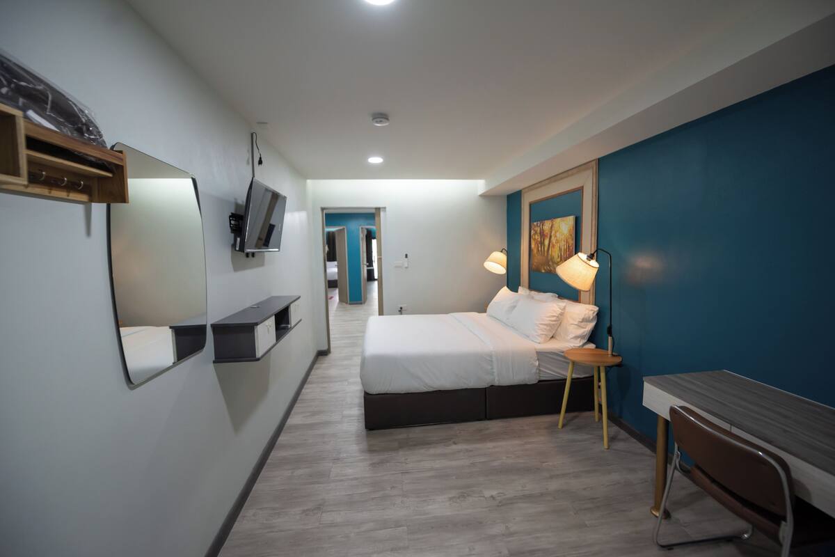 A modern hotel room with a bed, bedside table, lamp, and a TV mounted on the wall.