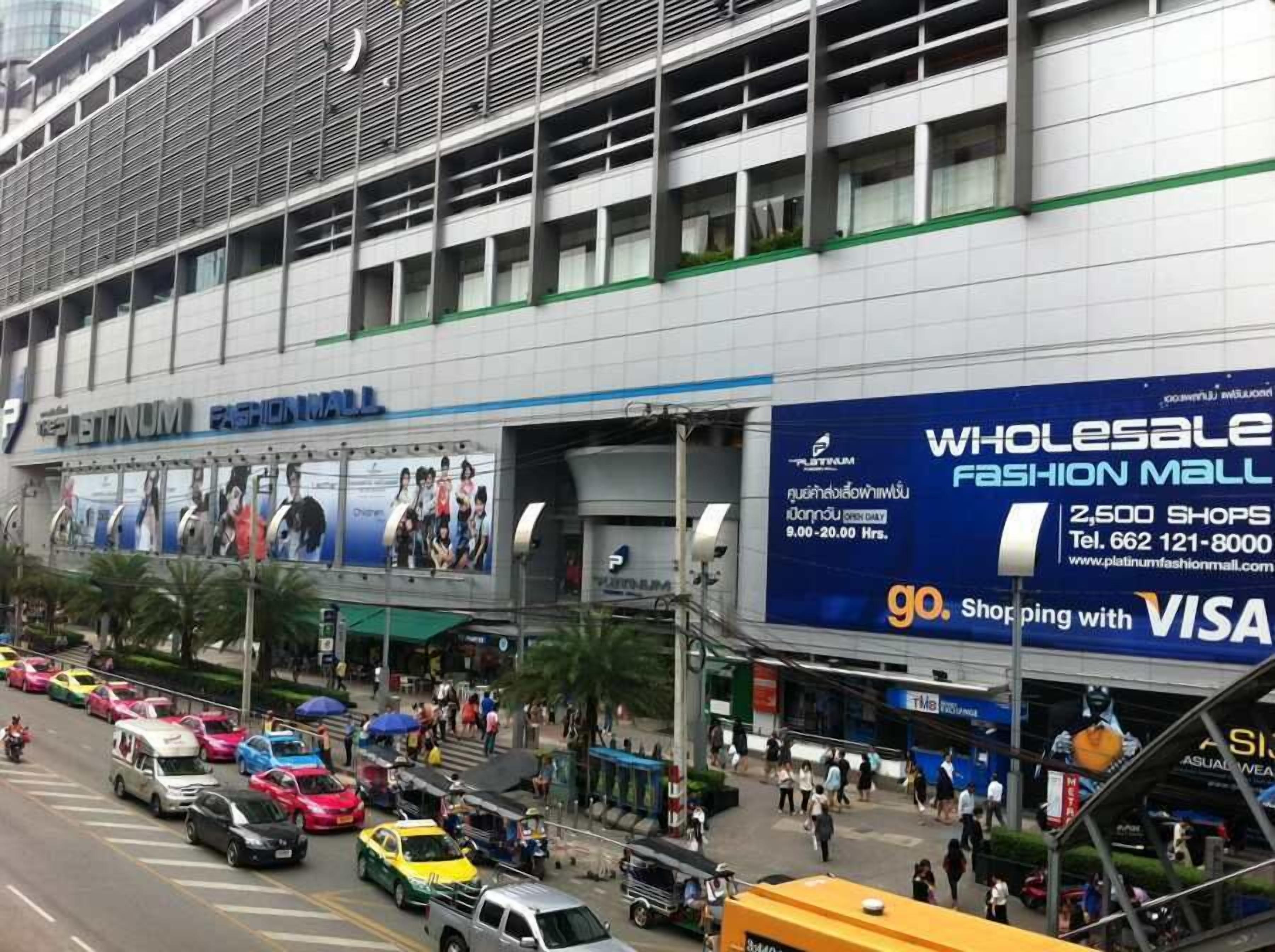 A busy street with a large building labeled "Platinum Fashion Mall" featuring a blue sign advertising wholesale shops and VISA card acceptance.