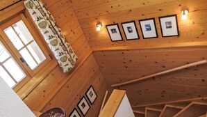 A wooden interior with a staircase, a window with curtains, and framed pictures on the wall.