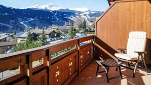 A wooden balcony with a view of snow-capped mountains, a chair, and a table.