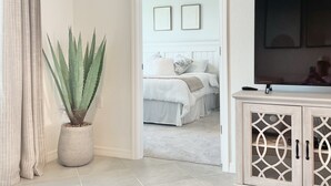 A hotel room with a bed, a potted plant, a television, and a cabinet with decorative glass panels. - Picturesque Punta Gorda Condo on Golf Course with Nature Preserve Views! (Punta Gorda)