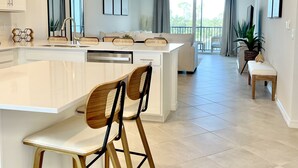 A modern kitchen with a central island, bar stools, and a dining area with a bench. - Picturesque Punta Gorda Condo on Golf Course with Nature Preserve Views! (Punta Gorda)