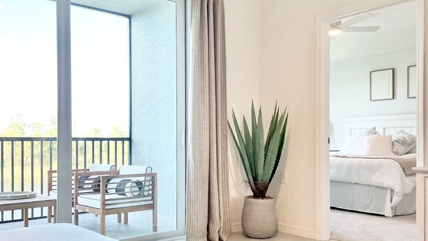 A modern room with a balcony, a potted plant, a bed, and a seating area. - Picturesque Punta Gorda Condo on Golf Course with Nature Preserve Views! (Punta Gorda)