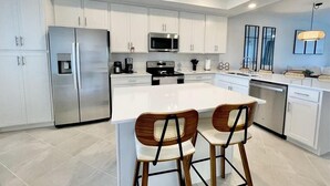 A modern kitchen with white cabinets, stainless steel appliances, and a central island with two bar stools. - Picturesque Punta Gorda Condo on Golf Course with Nature Preserve Views! (Punta Gorda)