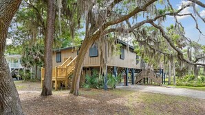 A wooden cabin with a porch and a staircase leading to the upper level. - 1 Block to Beach - Huge Screen Porch & Lagoon view (Edisto Island)
