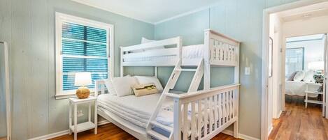 A bunk bed room with a window, a bedside table, and a lamp.