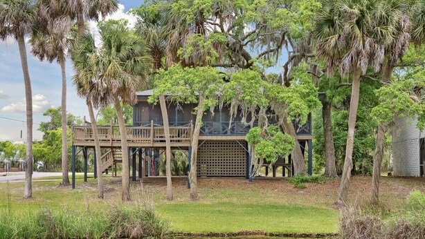 A wooden house with a deck, surrounded by palm trees and a pond. - 1 Block to Beach - Huge Screen Porch & Lagoon view (Edisto Island)