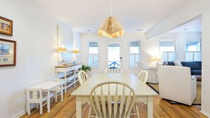 A bright dining area with a white table and chairs, a hanging light fixture, and a view of the outdoors through windows. - 1 Block to Beach - Huge Screen Porch & Lagoon view (Edisto Island)