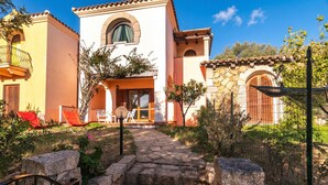 A Mediterranean-style building with a stone pathway leading to a door, surrounded by greenery and outdoor seating. - Quiet Sanibel, Monte Petrosu, Italy (Monte Petrosu)