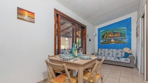 Un comedor con una mesa y sillas de madera, un cuadro en la pared y vistas a través de un ventanal.