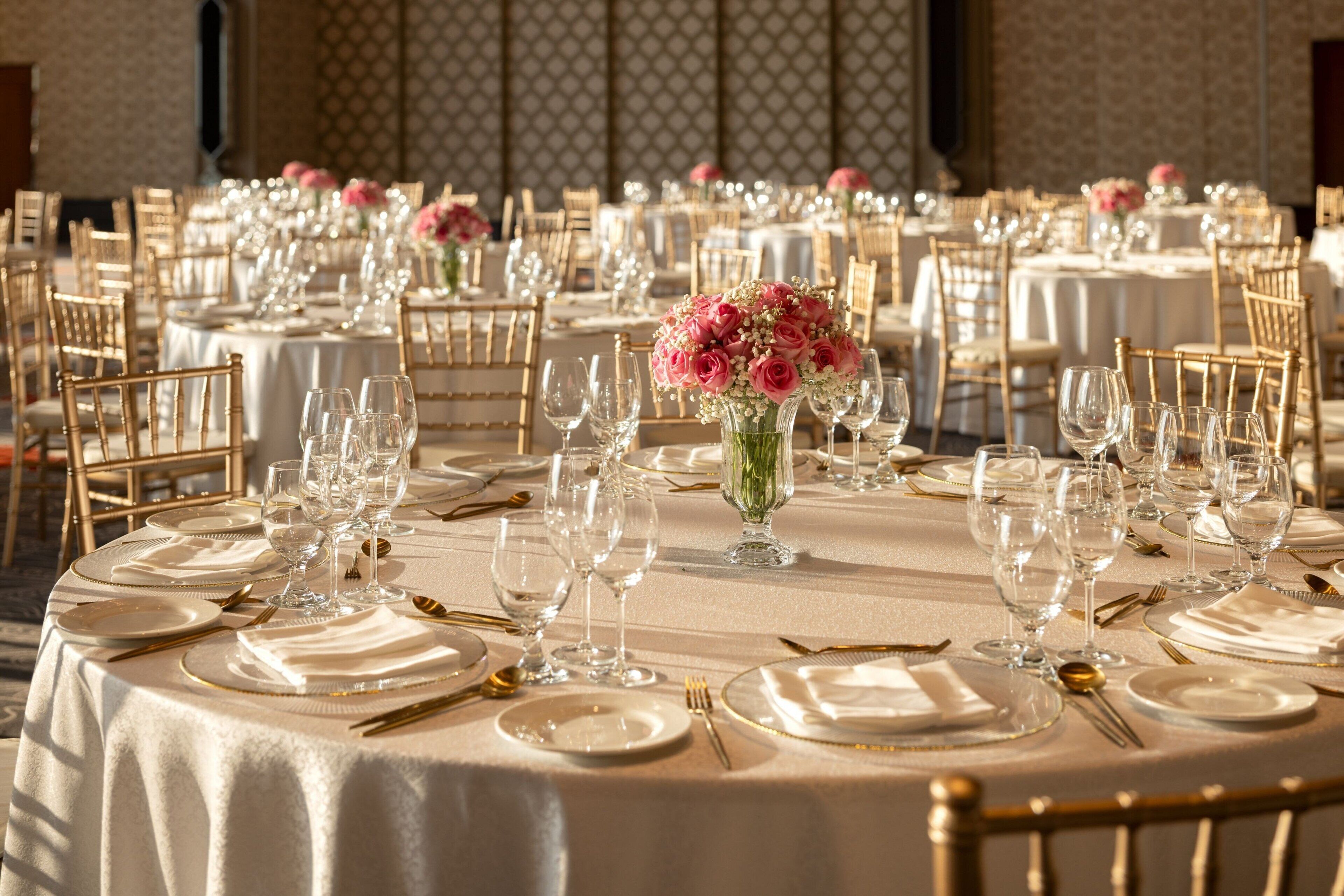 En festlokal med runda bord uppdukade för middag, där varje bord har vita dukar, guldfärgade bestick och klara glas.
