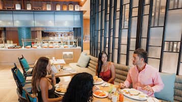 A group of people dining in a modern hotel restaurant with a view of the kitchen and a large window with a grid pattern.