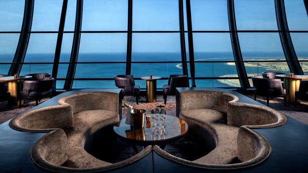 A modern lounge with a curved seating arrangement, a central table with a bottle and glasses, and a large window offering a view of the sea and distant land. - ITC Ratnadipa, a Luxury Collection Hotel, Colombo (Colombo)