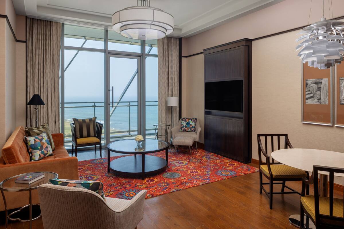 A modern living room with a large window, a round coffee table, a sofa, and a dining area.