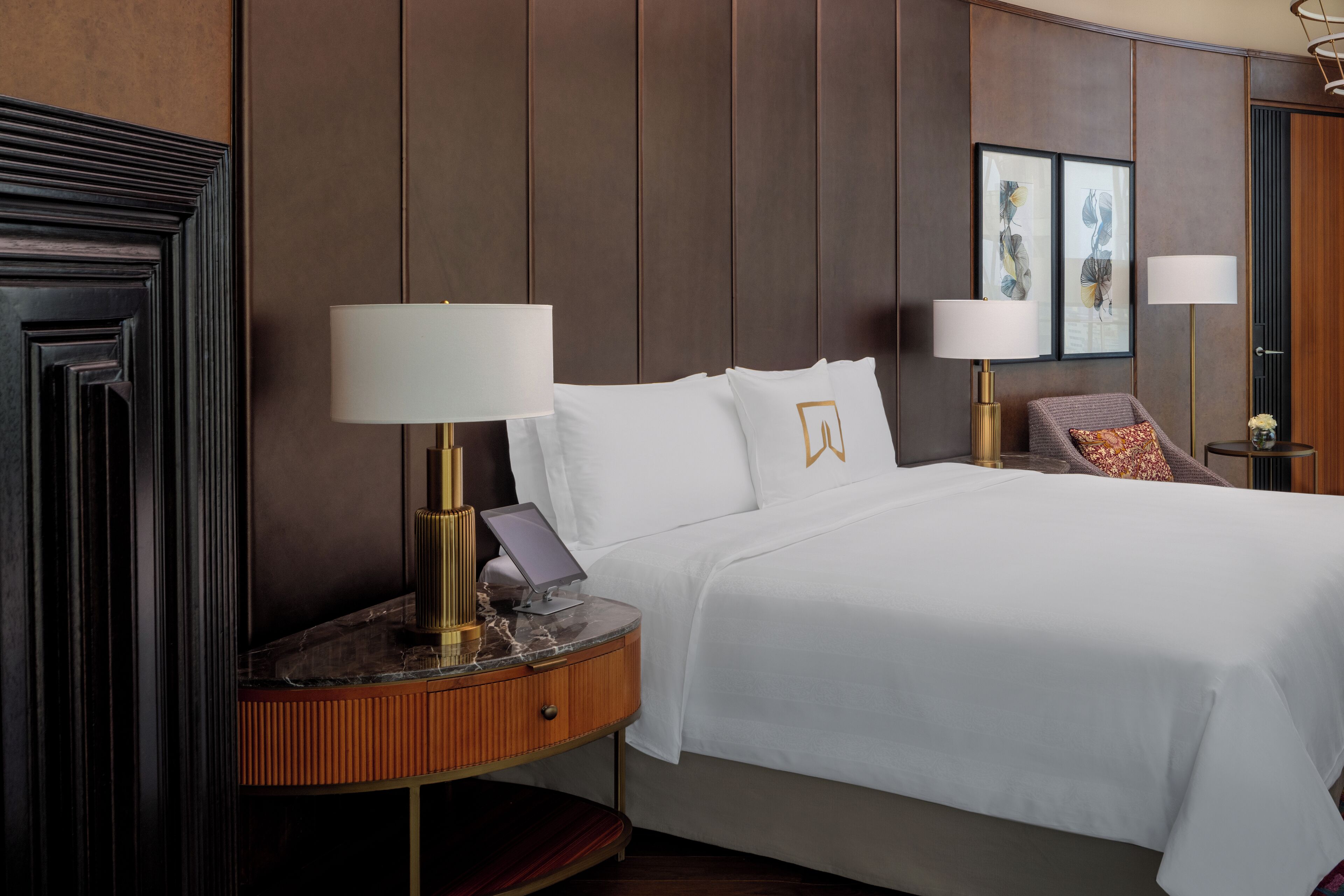 A hotel room with a large bed, two bedside lamps, a small table with a lamp, and a wall-mounted artwork.