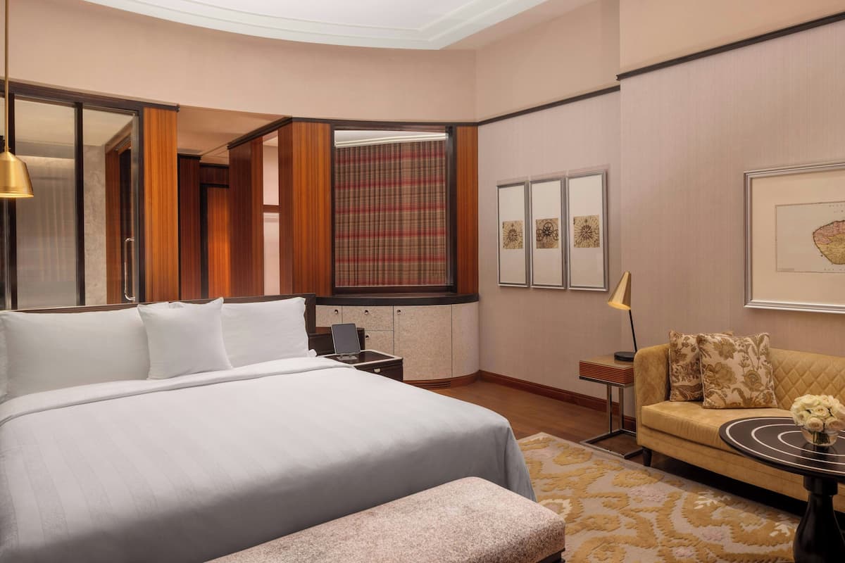 A hotel room with a large bed, a sofa, a desk with a laptop, a mirror, and framed artwork on the wall.