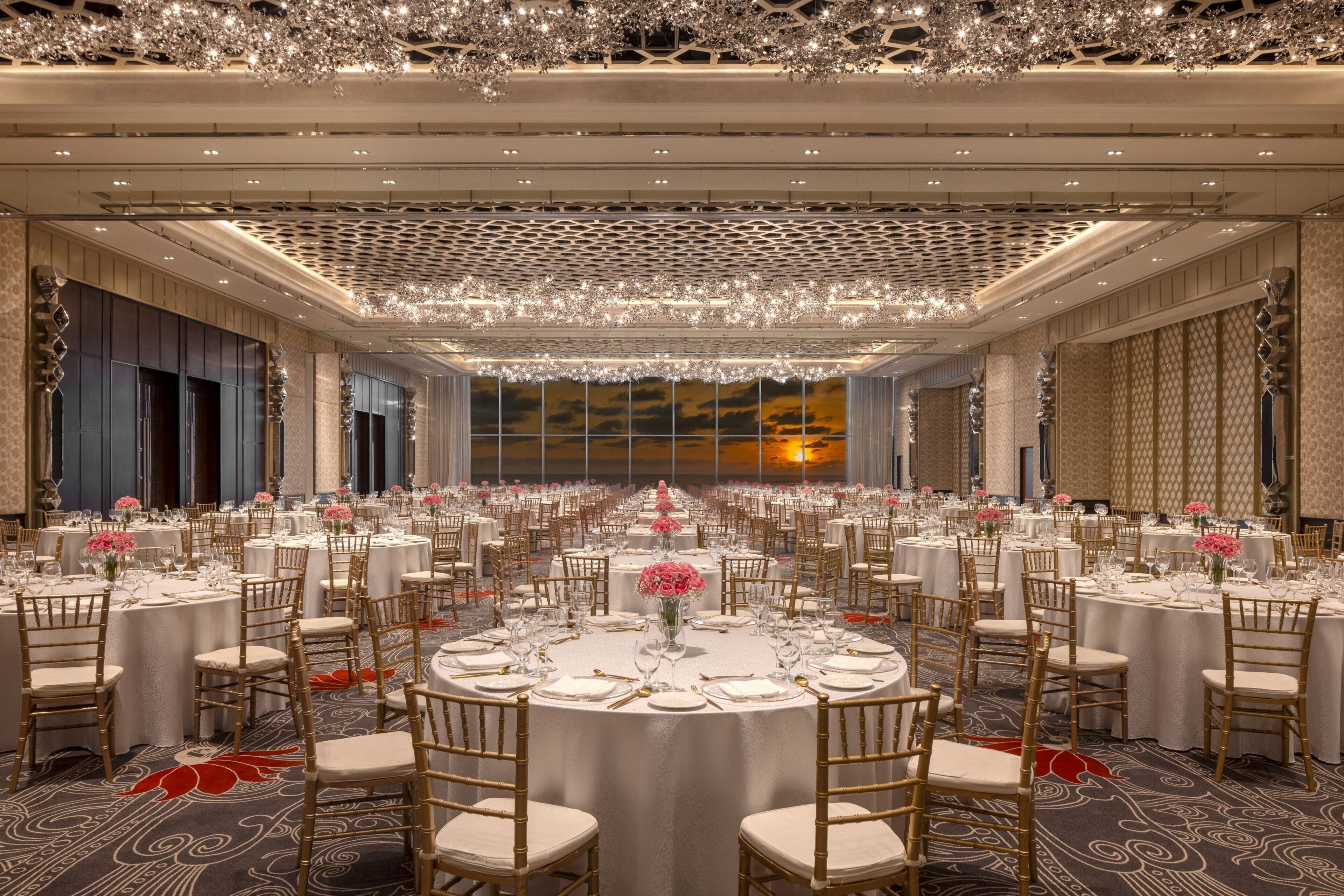 A banquet hall with round tables, chairs, and chandeliers.