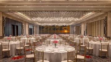 A banquet hall with round tables, chairs, and chandeliers.