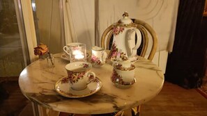 Une table dressée avec un service à thé comprenant une théière, des tasses et des soucoupes, dans une pièce dotée d’un plancher en bois et d’une chaise avec un dossier décoratif.
