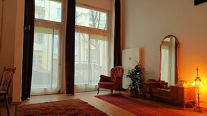 Tilava olohuone, jossa on suuri ikkuna, punainen nojatuoli, puinen kaappi ja lattiavalaisin.