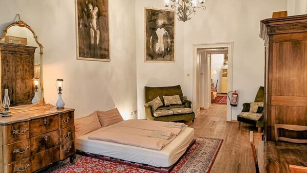 Une chambre à coucher avec un lit, une commode et deux chaises. Les murs sont ornés de tableaux et un lustre est suspendu au plafond.