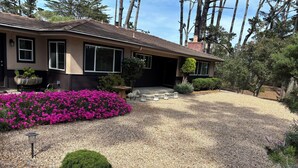 A house with a gravel driveway, a flower bed with pink flowers, and a well-maintained garden. -  Gracious 3-bedroom Pebble Beach Home in Quiet, Convenient Wooded Area (Del Monte Forest)