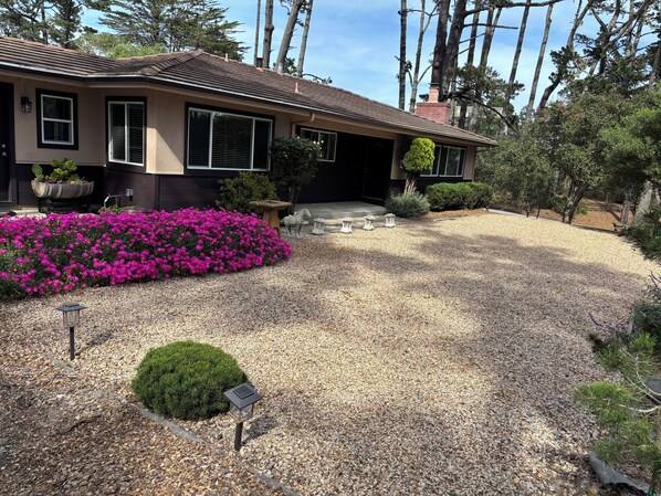A house with a gravel driveway, a flower bed with pink flowers, and a well-maintained garden. -  Gracious 3-bedroom Pebble Beach Home in Quiet, Convenient Wooded Area (Del Monte Forest)