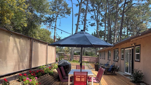 A wooden deck with a table and chairs, a barbecue grill, and a covered area with an umbrella. -  Gracious 3-bedroom Pebble Beach Home in Quiet, Convenient Wooded Area (Del Monte Forest)