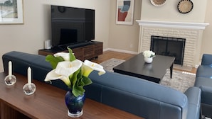 A living room with a blue sofa, a coffee table, a TV, and a fireplace. -  Gracious 3-bedroom Pebble Beach Home in Quiet, Convenient Wooded Area (Del Monte Forest)