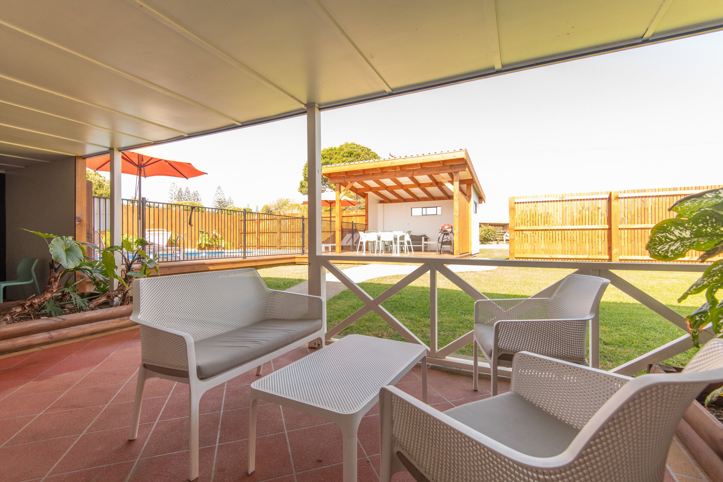 Un patio cubierto con muebles de mimbre, una cerca de madera y un edificio pequeño al fondo.