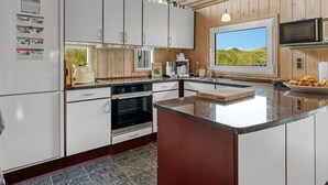 Une cuisine moderne avec des armoires blanches, un grand îlot central, un four encastré et une fenêtre donnant sur l’extérieur.