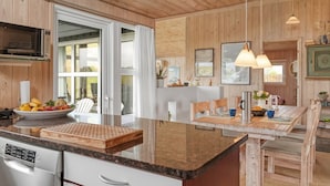 Une cuisine moderne avec un lambris en bois, un grand îlot central doté d’un lave-vaisselle intégré, un éclairage suspendu et une vue sur l’extérieur.