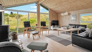 Un vaste espace de vie doté de planchers en bois, de grandes fenêtres, d’une cheminée et de meubles modernes.