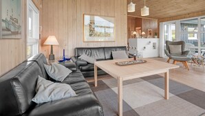 Un salon chaleureux avec un plafond en bois, un canapé en cuir noir, une table basse en bois et un tableau encadré au mur.