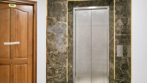 Un couloir avec une porte en bois portant l’inscription « 501 » et un ascenseur dont la paroi est recouverte de marbre et qui est doté d’un écran numérique affichant le chiffre « 3 ».