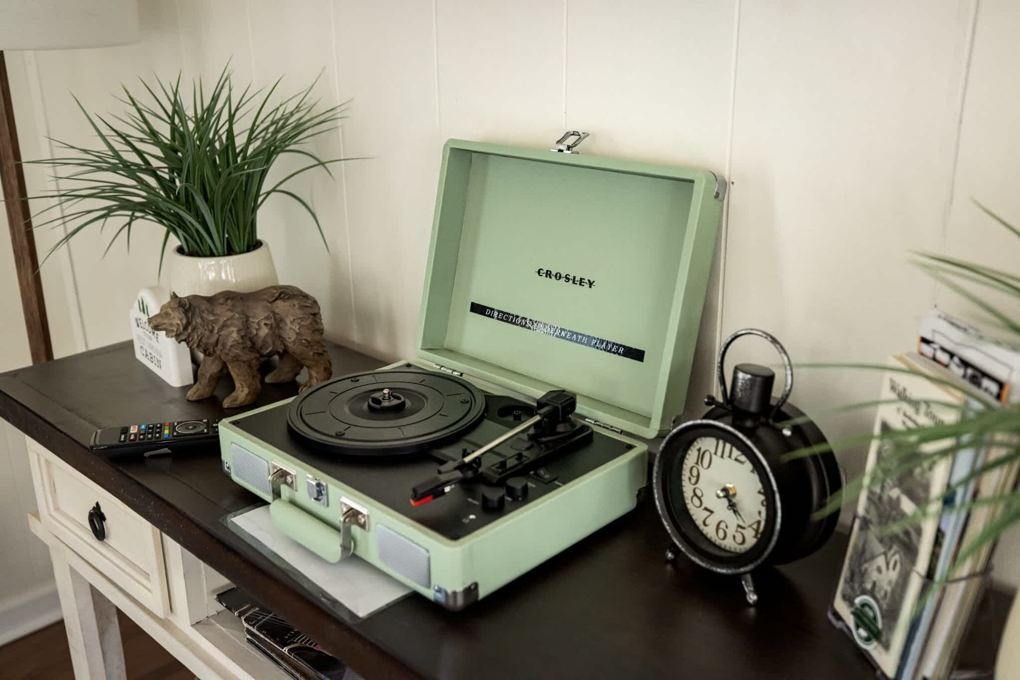 Un tourne-disque de style rétro posé sur un bureau, avec une plante, une petite figurine et une horloge.