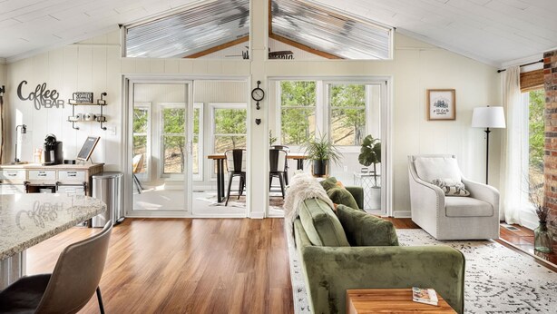 A spacious living area with a kitchen, dining table, and a green sofa. - 2BR cabin w/ hot tub & workspace (Hedgesville)