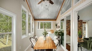 A dining area with a wooden table and chairs, large windows, and a brick wall. - 2BR cabin w/ hot tub & workspace (Hedgesville)
