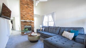 A modern living room with a grey sofa, a round coffee table, and a brick fireplace. - Cheerful 2 Bedroom Home near Virginia Wesleyan (Virginia Beach)