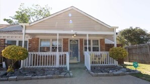 A two-story house with a front porch, brick exterior, and a small front yard with two bushes. - Cheerful 2 Bedroom Home near Virginia Wesleyan (Virginia Beach)