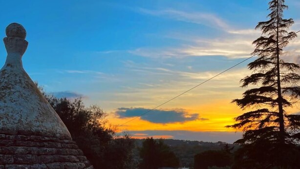 A terrace with a view of a sunset, a stone chimney, and a table with a tray of snacks and drinks. - Vole  Authentic trullo in Itria valley (CEGLIE MESSAPICA)