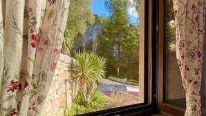 A window with floral curtains, a stone ledge, and a view of greenery and trees outside. - Vole  Authentic trullo in Itria valley (CEGLIE MESSAPICA)