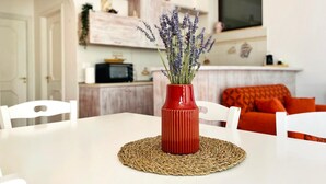 A dining area with a white table, a red vase with lavender, and a woven placemat. - Vole  Authentic trullo in Itria valley (CEGLIE MESSAPICA)