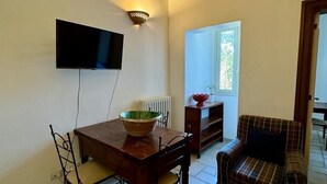 Un comedor con una mesa de madera, sillas, un cuenco, un televisor montado en la pared y un ventanal con vistas a follaje.