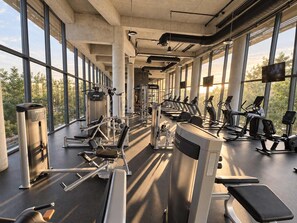 A gym with cardio machines, weight stations, and large windows offering a view of the outdoors.