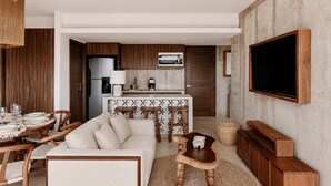 A modern living room with a sofa, coffee table, and dining area with chairs and a table set for a meal. - Paradise Penthouse | Cenote, Rooftop Pool & Sauna (Tulum)