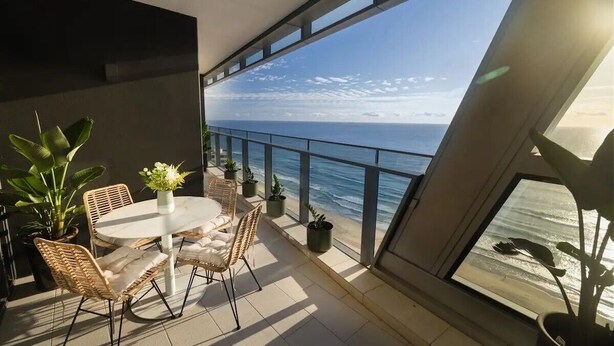 A balcony with a view of the ocean, furnished with a table and chairs, and surrounded by potted plants.