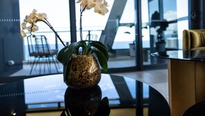 A modern interior with a glass table, a vase with orchids, and a view of the sea through large windows.